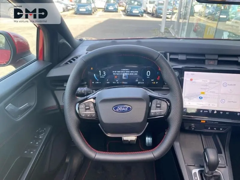 Vue intérieure centrée sur le volant multifonction de la Ford Puma rouge, avec tableau de bord numérique et écran tactile.