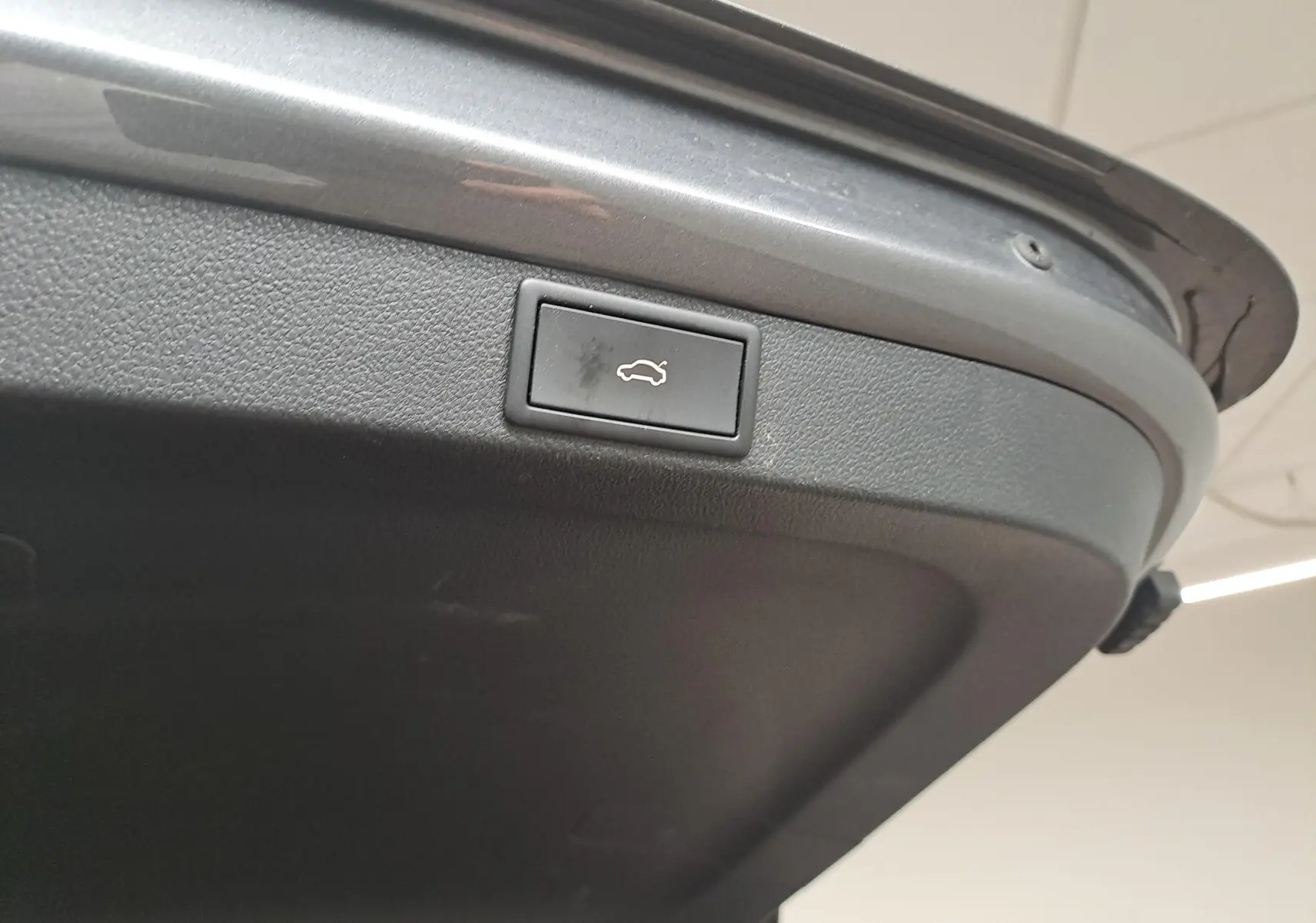 Gros plan sur le bouton d'ouverture électrique du coffre, intégré dans le hayon gris graphite d'une Skoda Octavia Combi 2024.