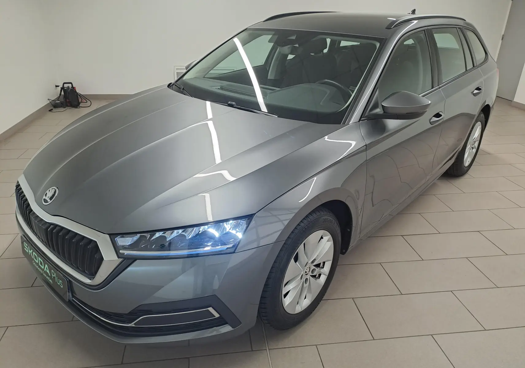 Vue 3/4 avant droite d'une Skoda Octavia Combi 2024 gris graphite métallisé avec phares allumés en intérieur.