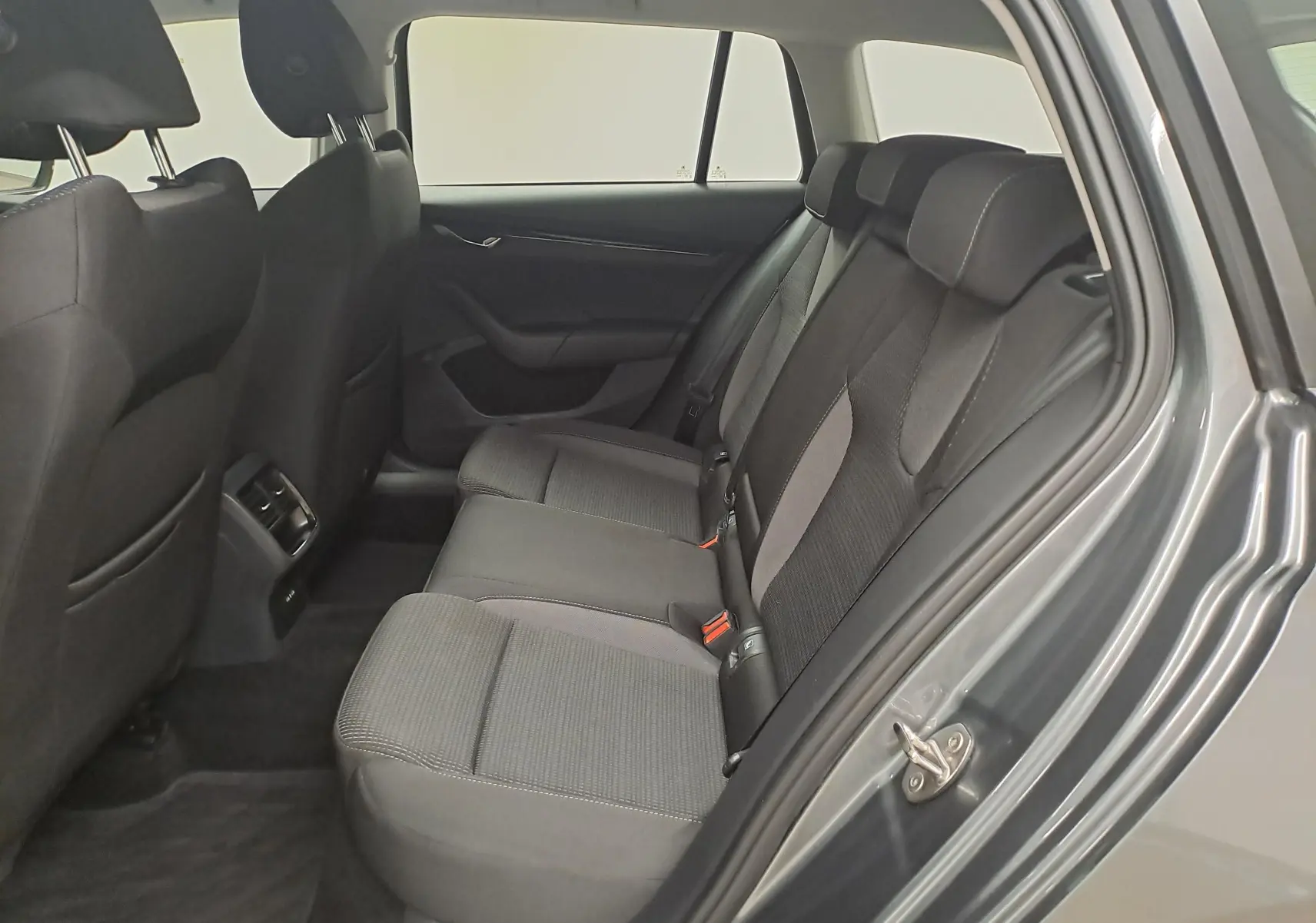 Vue intérieure arrière droite de la Skoda Octavia Combi 2024 gris graphite, montrant les sièges arrière en tissu noir et gris.