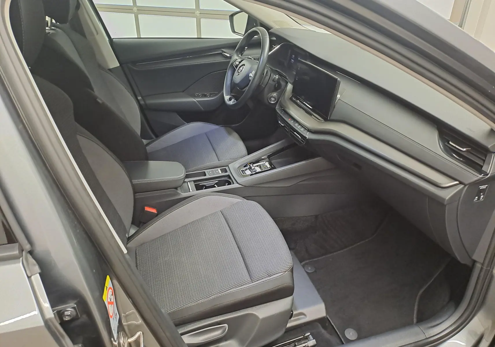 Vue intérieure côté conducteur de la Skoda Octavia Combi 2024, sièges tissu gris et tableau de bord moderne noir.