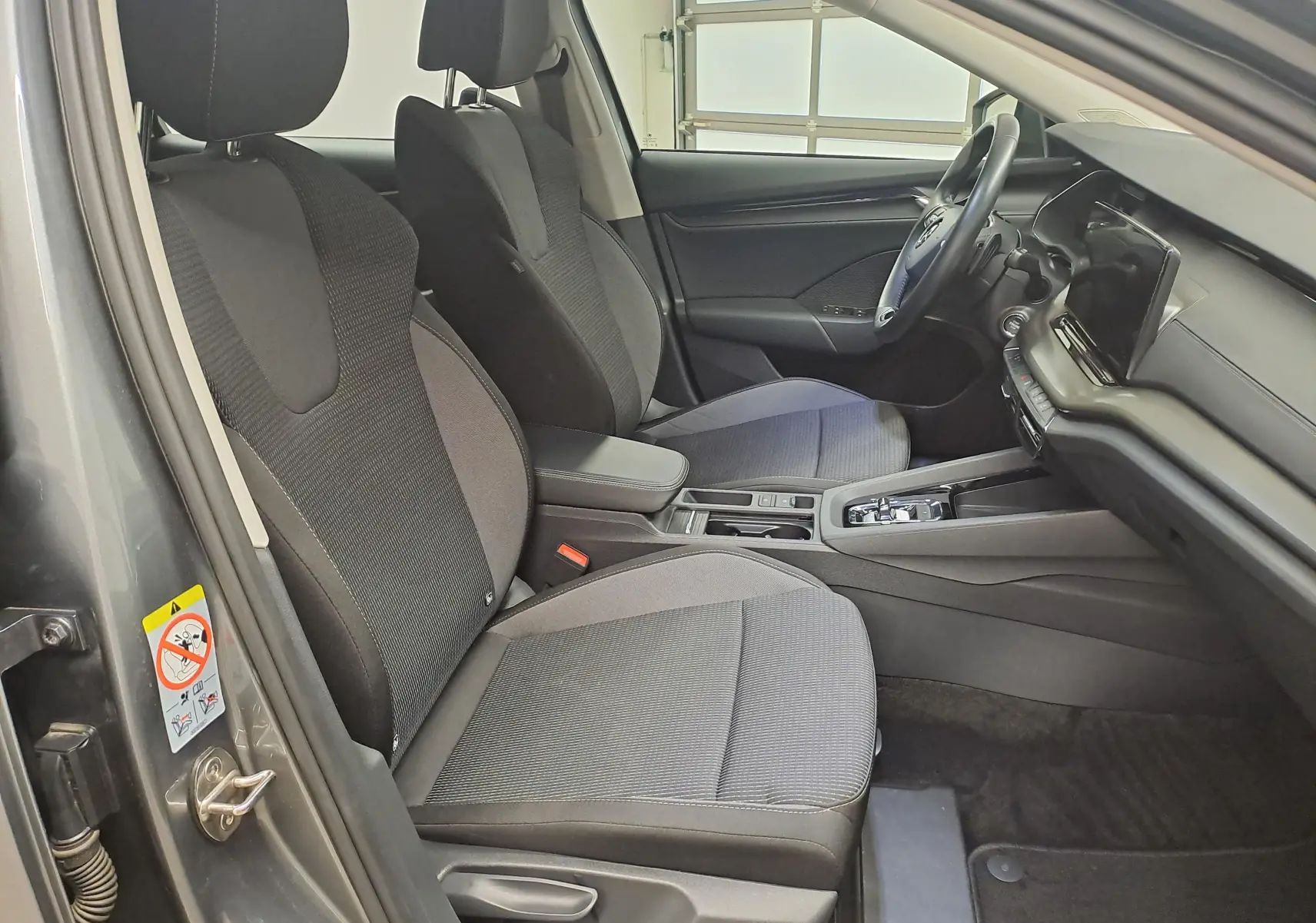 Intérieur avant de la Skoda Octavia Combi 2024 gris graphite, vue côté conducteur avec sièges tissu et tableau de bord moderne.