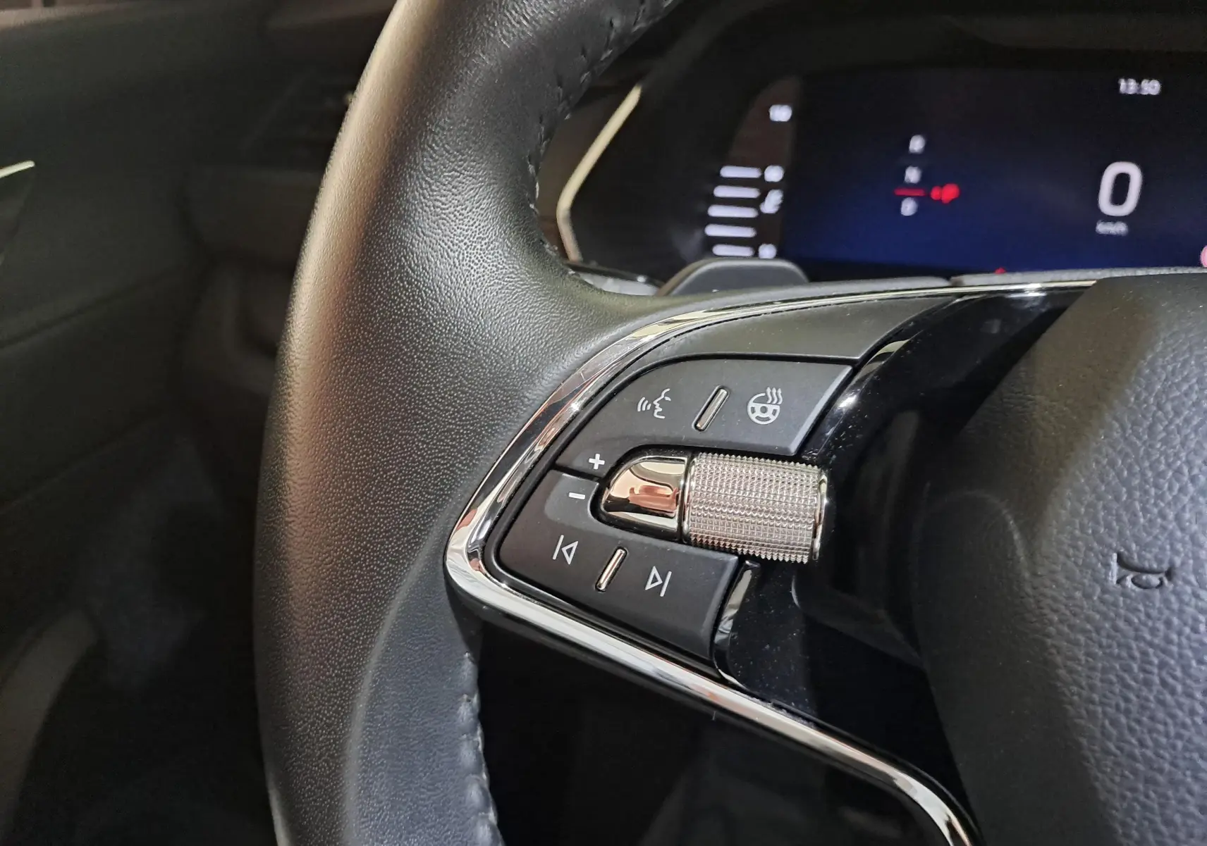 Gros plan sur les commandes gauche du volant en cuir noir du Skoda Octavia Combi 2024, avec molette métallique et tableau de bord numérique.