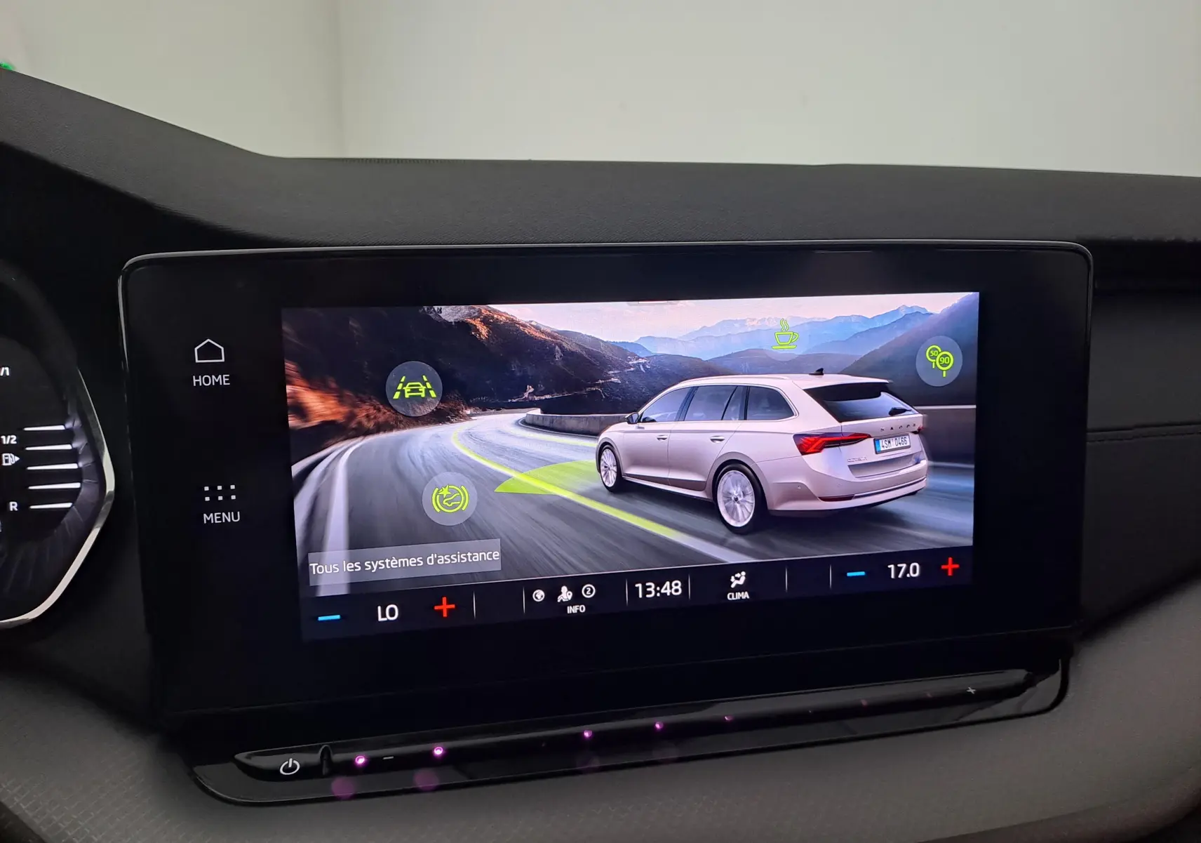 Écran tactile montrant une Skoda Octavia Combi gris graphite vue de trois quarts arrière sur une route sinueuse.