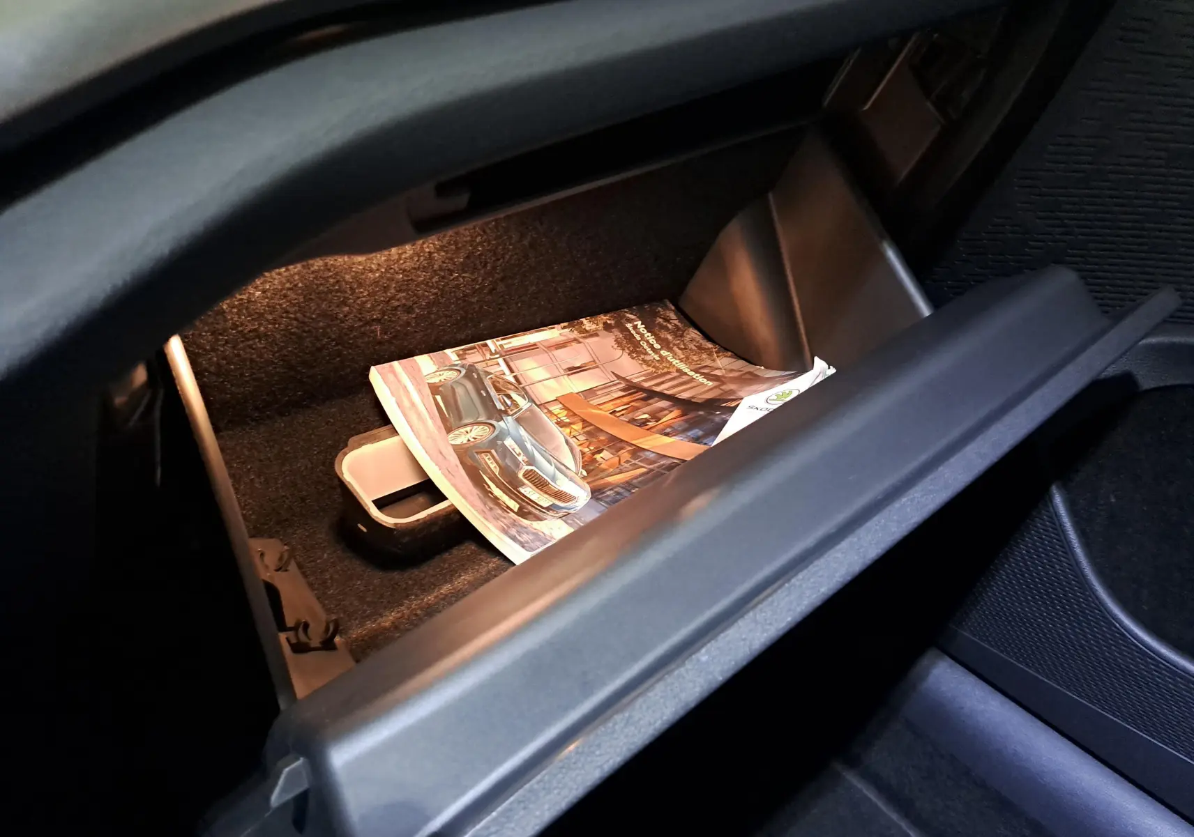 Gant de boîte à gants ouvert avec manuel du Skoda Octavia Combi 1.5 eTSI 150 DSG7 Business visible à l'intérieur.