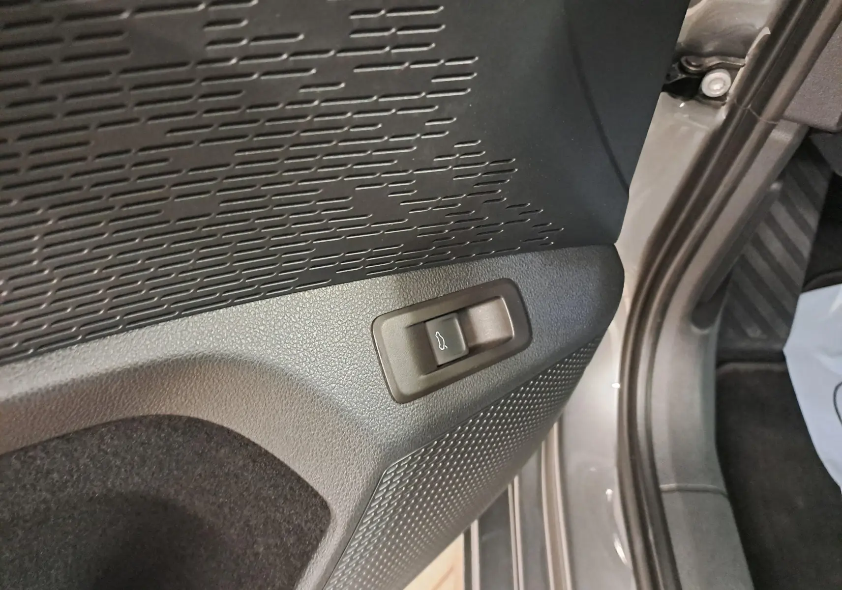 Gros plan sur le bouton d'ouverture électrique du coffre dans l'habitacle gris graphite d'une Skoda Octavia Combi 2024.