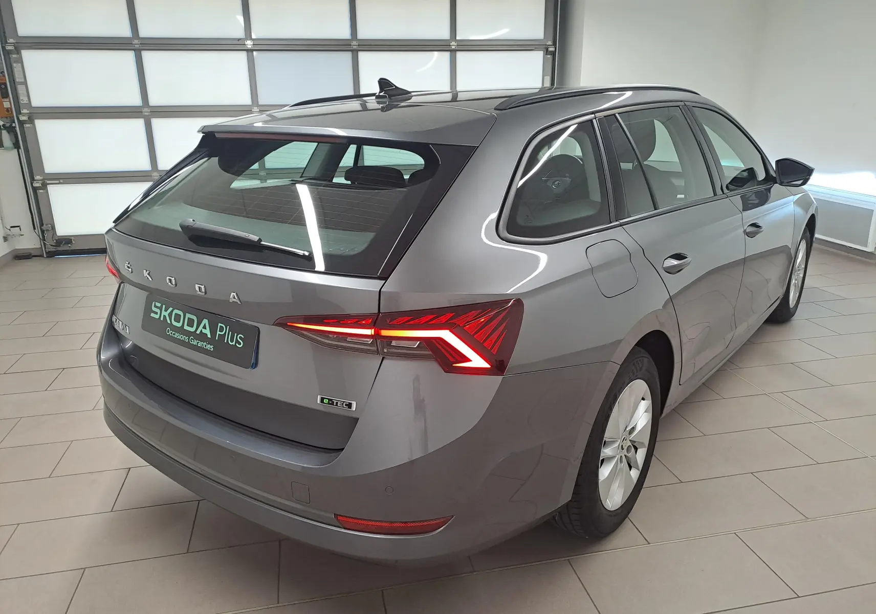 Vue 3/4 arrière droite d'une Skoda Octavia Combi 2024 gris graphite avec feux arrière LED allumés en intérieur showroom.