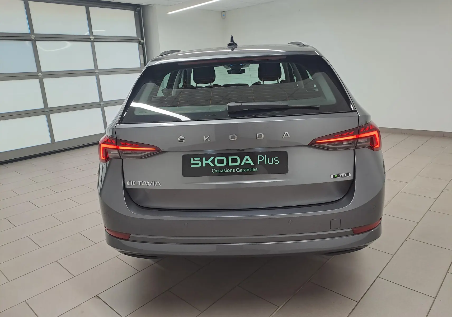 Vue arrière d'une Skoda Octavia Combi 2024 gris graphite avec feux LED allumés et logo e-TEC visible.