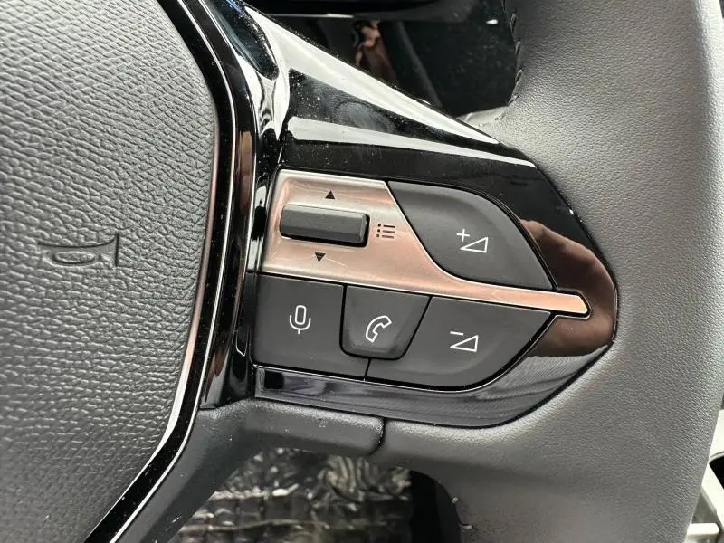 Gros plan sur les commandes multifonctions noires et argentées du volant de la Peugeot 308 hybride blanche.