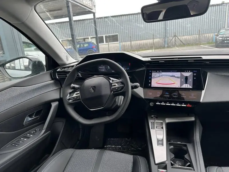Vue intérieure avant de la Peugeot 308 Hybrid 2025, tableau de bord noir avec écran tactile affichant la caméra de recul.