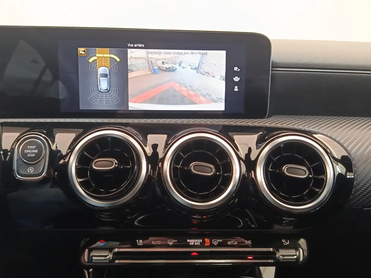 Vue intérieure du tableau de bord noir brillant de la Mercedes Classe A 180 d avec écran tactile et aérateurs ronds chromés.