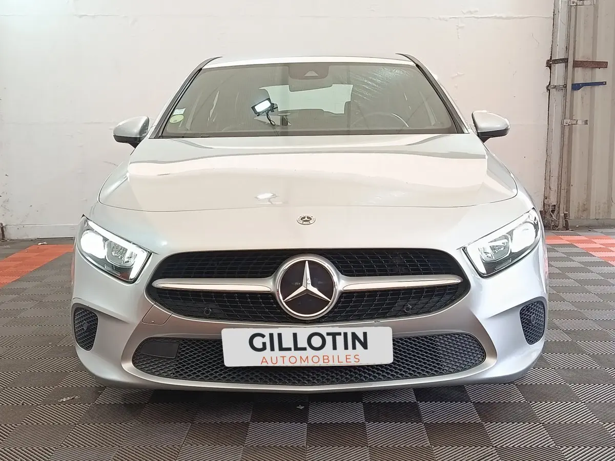 Vue frontale d'une Mercedes Classe A 180 d Business Line gris clair avec phares LED allumés et calandre distinctive.