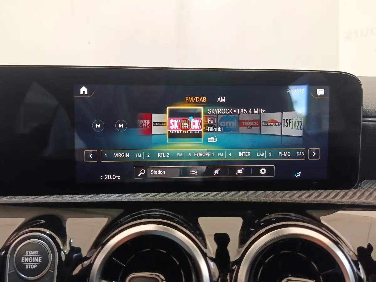 Écran tactile central allumé sur radio FM dans l’habitacle d’une Mercedes Classe A gris clair, vue de face rapprochée.