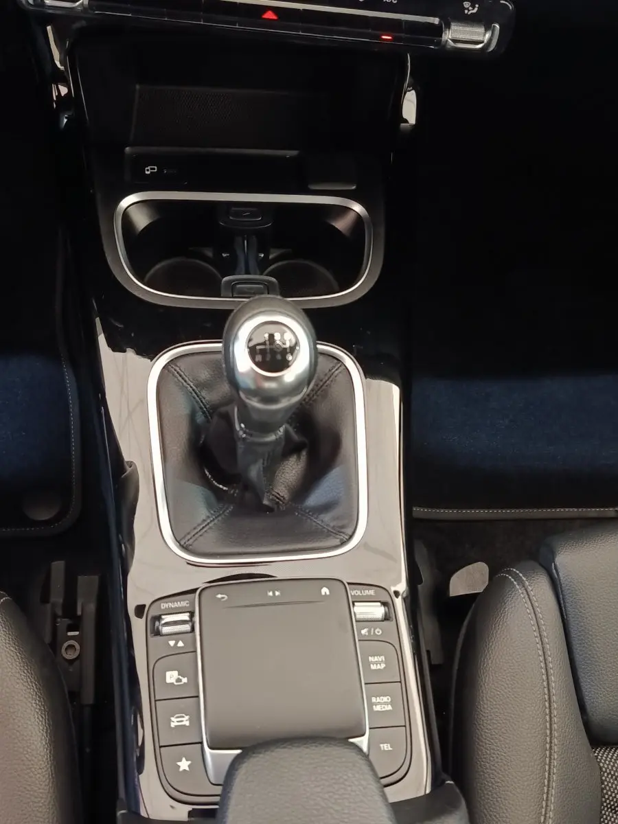 Vue rapprochée de la console centrale noire brillante avec levier de vitesses manuel et commandes tactiles d’une Mercedes Classe A gris clair.