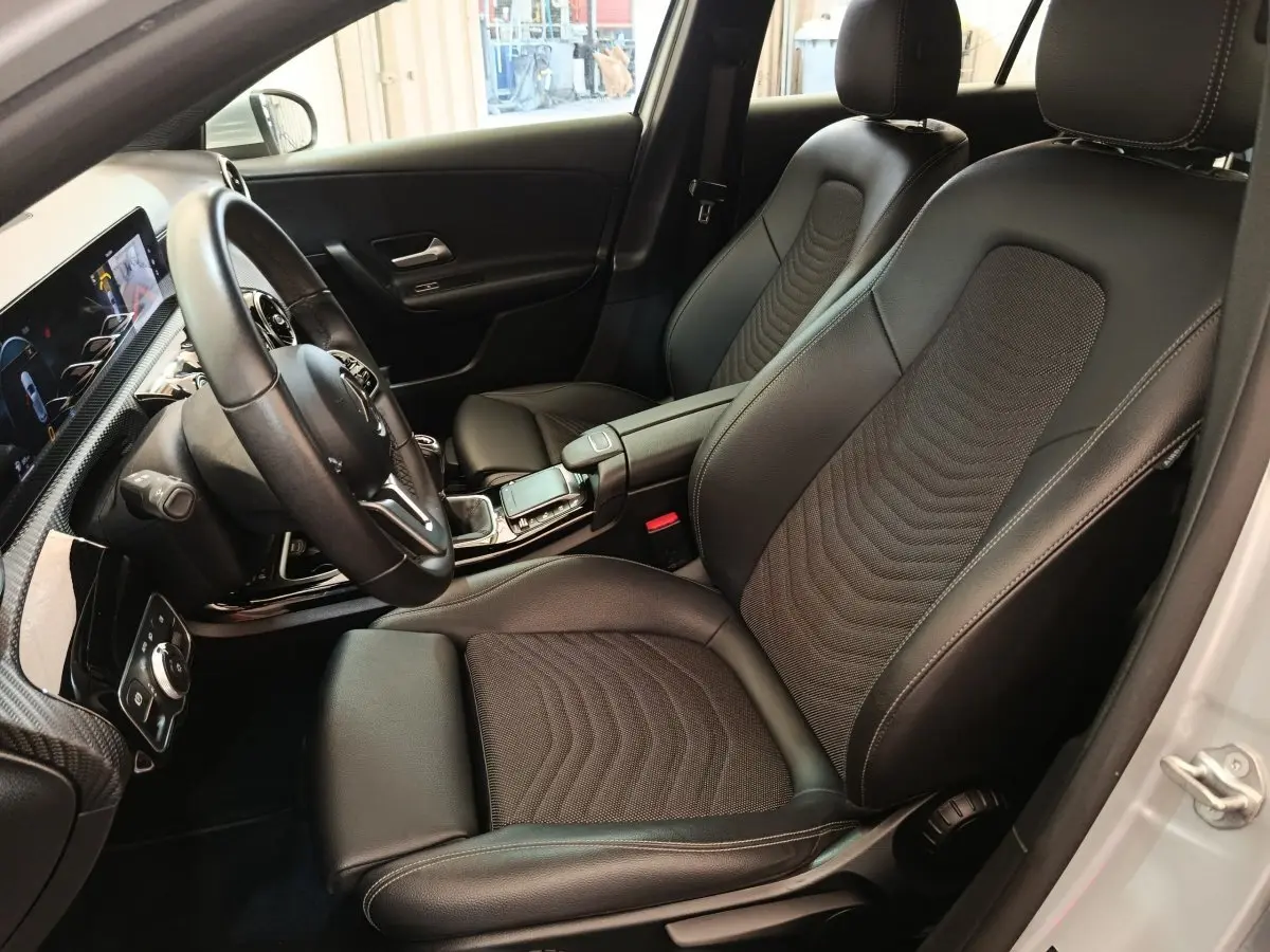 Vue intérieure côté conducteur de la Mercedes Classe A 180 d Business Line 2021 avec sièges cuir noirs et volant multifonctions.
