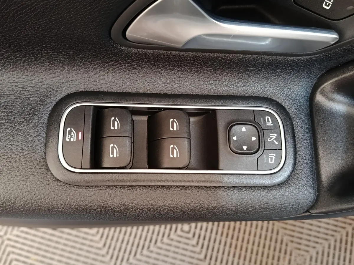 Gros plan sur les commandes des vitres électriques et rétroviseurs sur la porte côté conducteur d’une Mercedes Classe A gris clair.