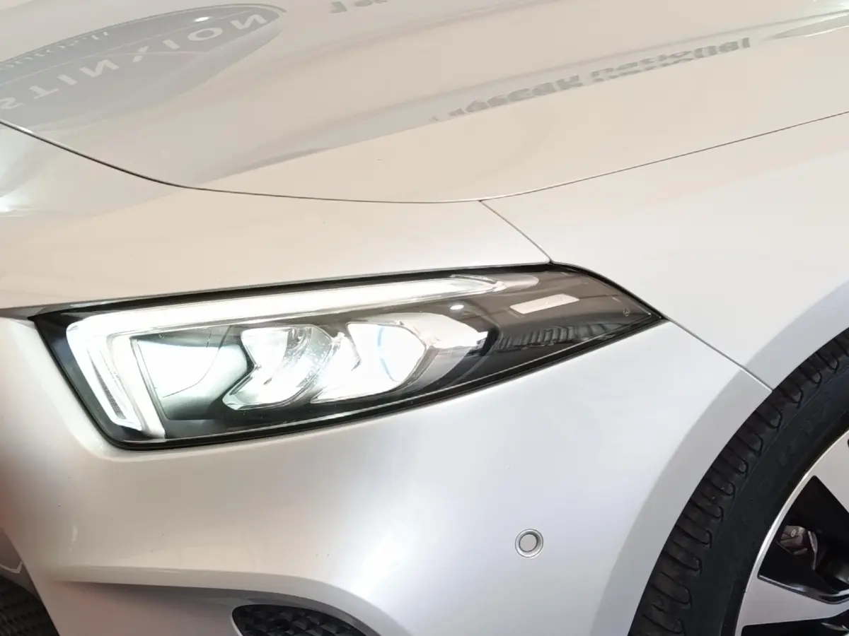 Gros plan sur l'avant droit gris clair d'une Mercedes Classe A 180 d Business Line avec phare LED allumé.
