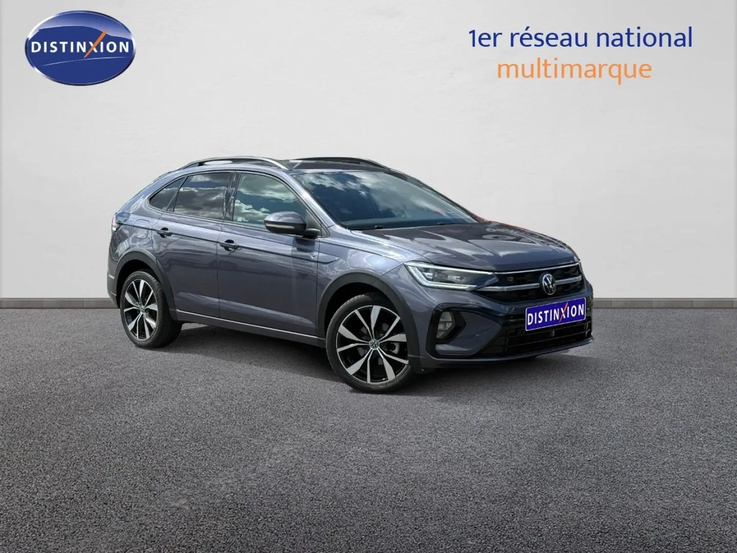 Volkswagen Taigo gris Ascot en 3/4 avant droit, avec jantes alu et barres de toit visibles.