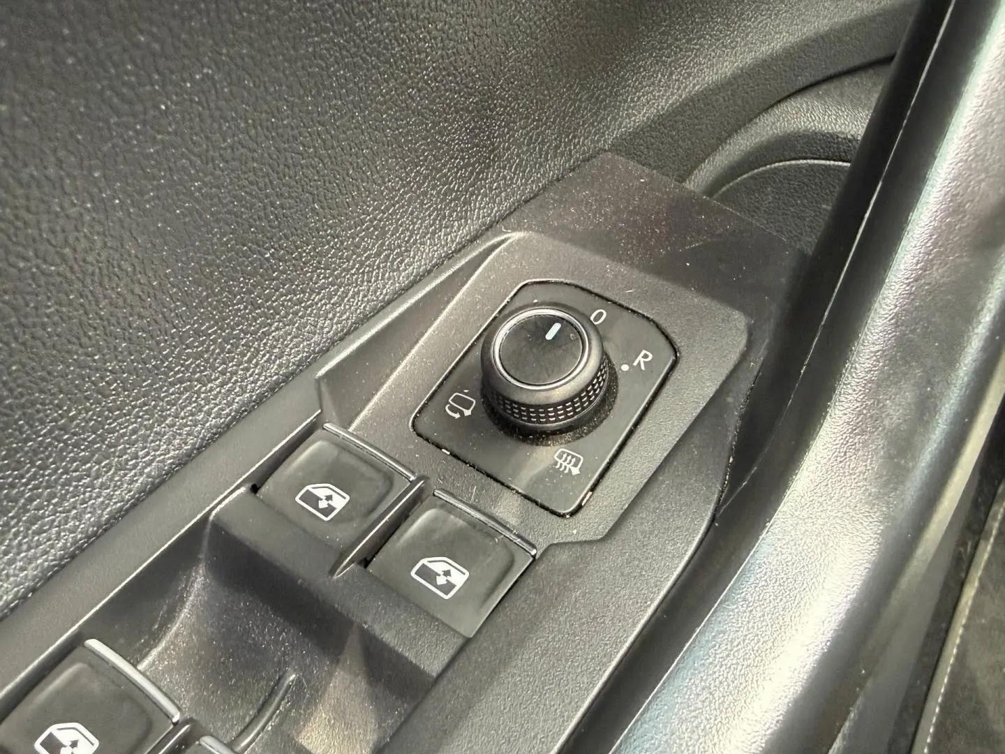 Gros plan sur les commandes de réglage des rétroviseurs et des vitres côté conducteur du Volkswagen Taigo gris.