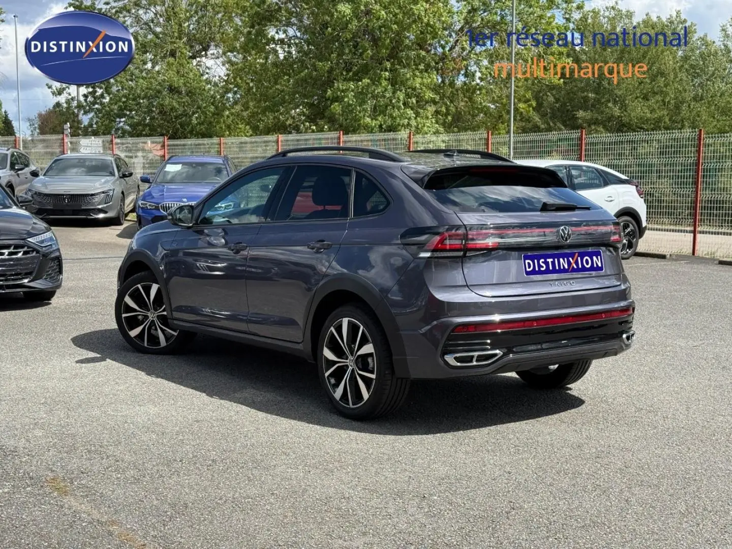Volkswagen Taigo gris Ascot en 3/4 arrière droit, avec jantes alliage et becquet arrière visible sur parking.