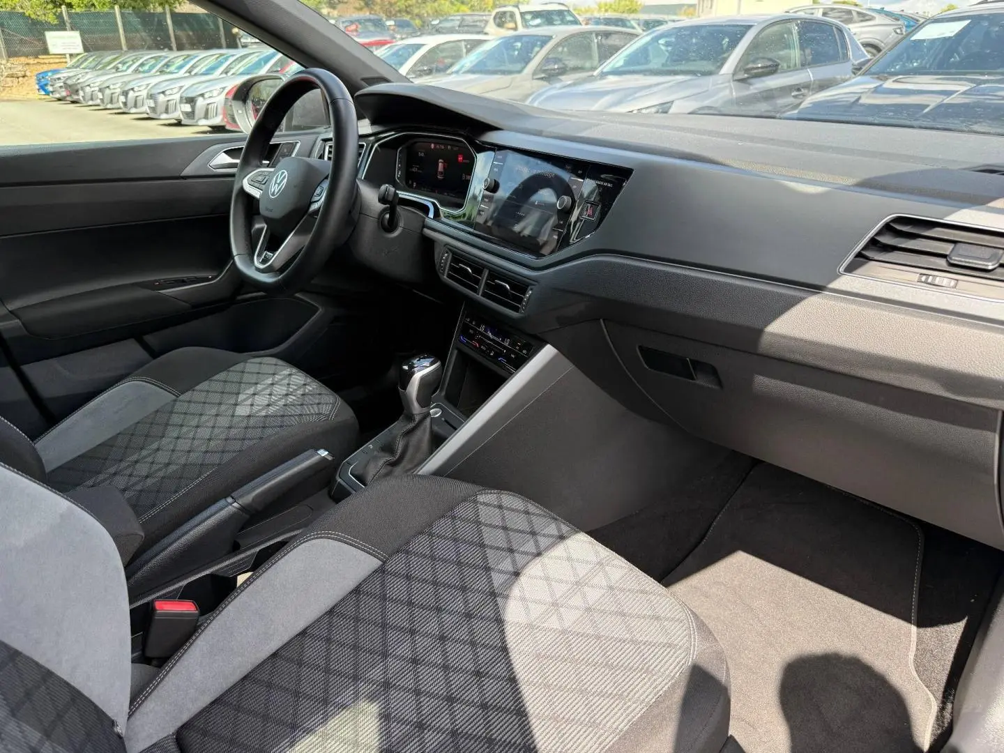 Vue intérieure côté conducteur du Volkswagen Taigo 2025, sièges tissu R-Line gris avec motifs, tableau de bord moderne noir.