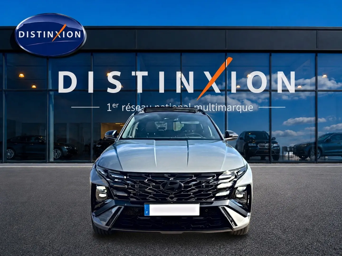 Vue frontale du Hyundai Tucson gris shadow 2026 avec calandre noire et feux LED distinctifs, devant une vitrine Distinxion.