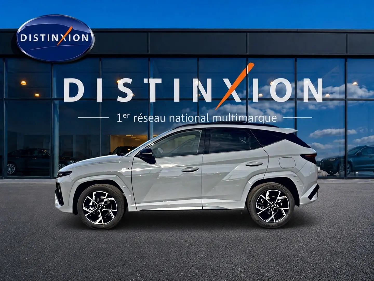 Hyundai Tucson 2026 gris shadow en profil droit devant vitrine Distinxion, jantes alu noires et toit noir.