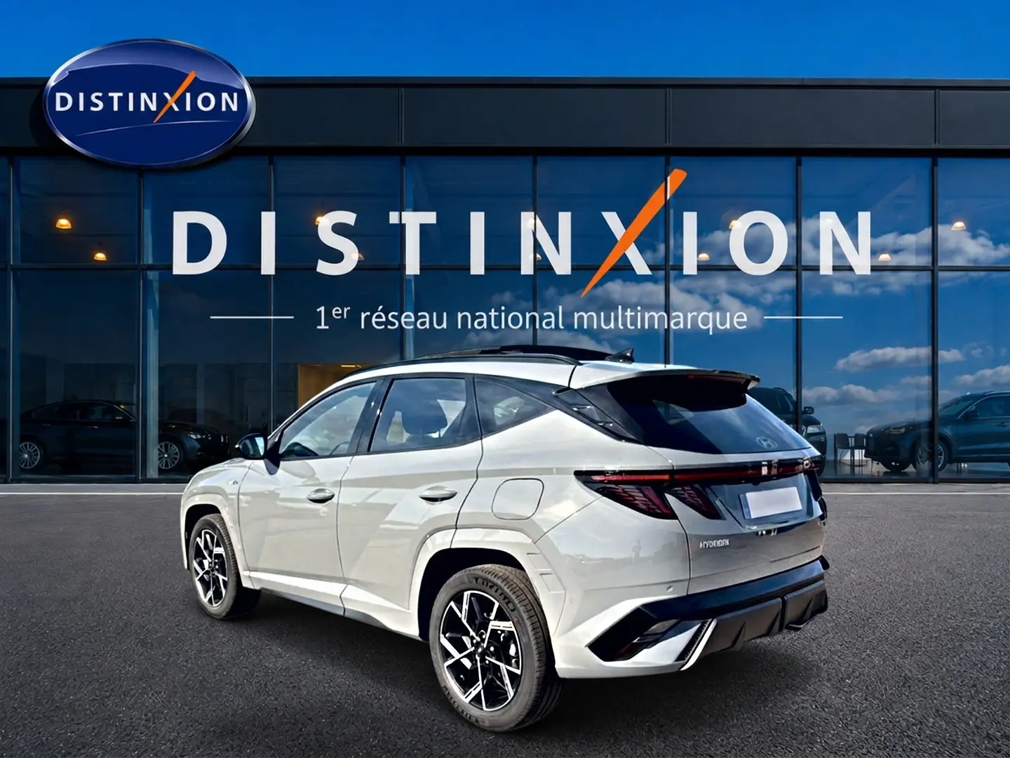 Vue 3/4 arrière droite du Hyundai Tucson 2026 gris shadow avec jantes alu et feux arrière LED, devant une vitrine Distinxion.