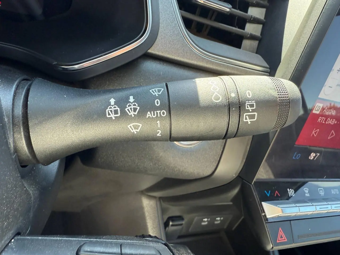 Gros plan sur la commande d’essuie-glace noire dans l’habitacle du Renault Captur gris métallisé, avec écran tactile visible.
