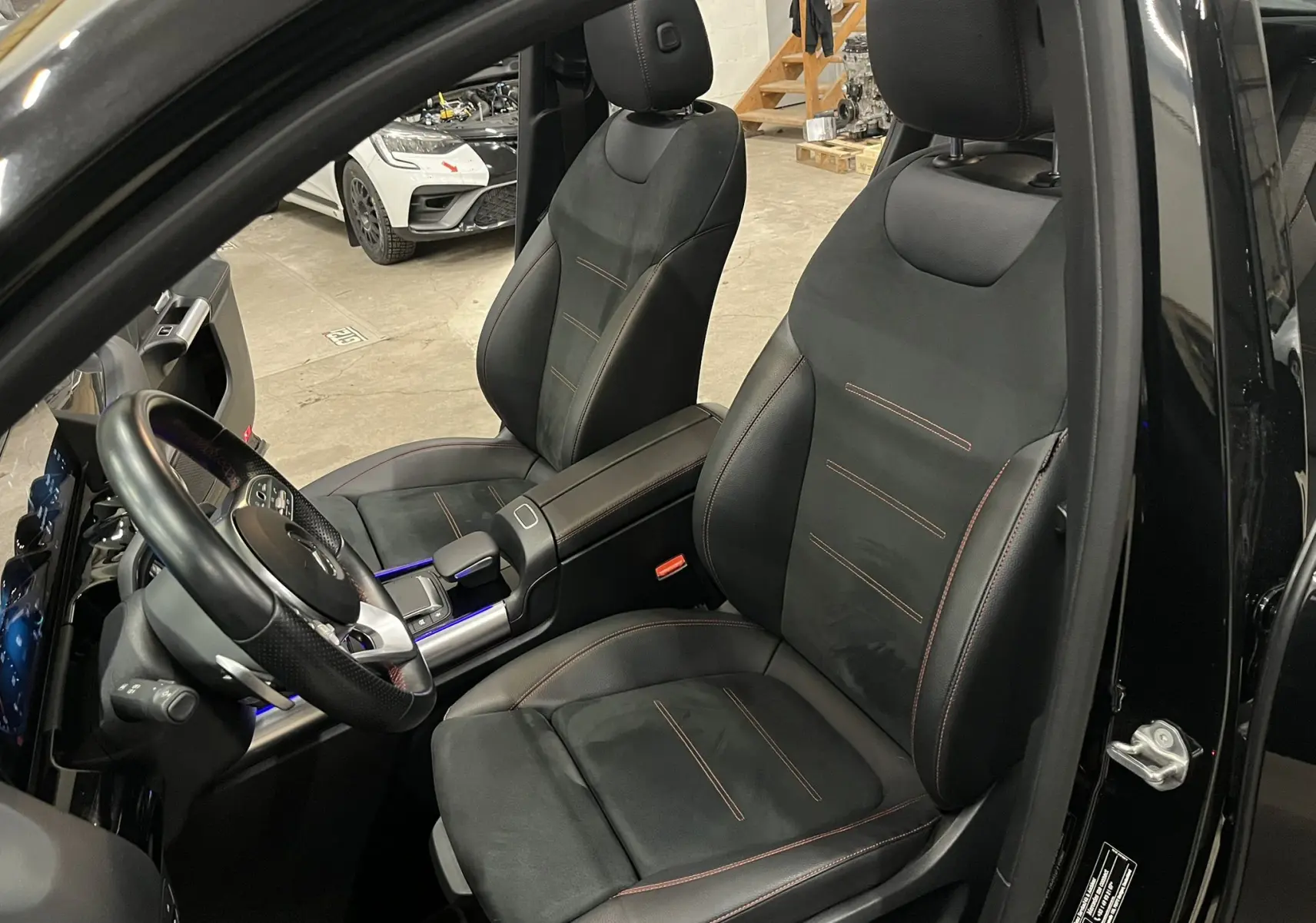 Vue intérieure côté conducteur du Mercedes GLA 250E AMG Line noir Cosmos avec sièges sport noirs et surpiqûres rouges.