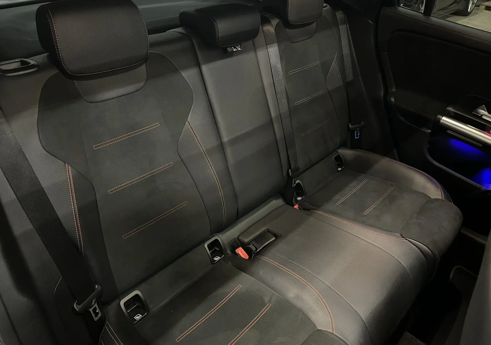 Vue intérieure arrière montrant les sièges noirs avec surpiqûres rouges et éclairage d'ambiance bleu sur porte d'une Mercedes GLA 250E AMG Line.