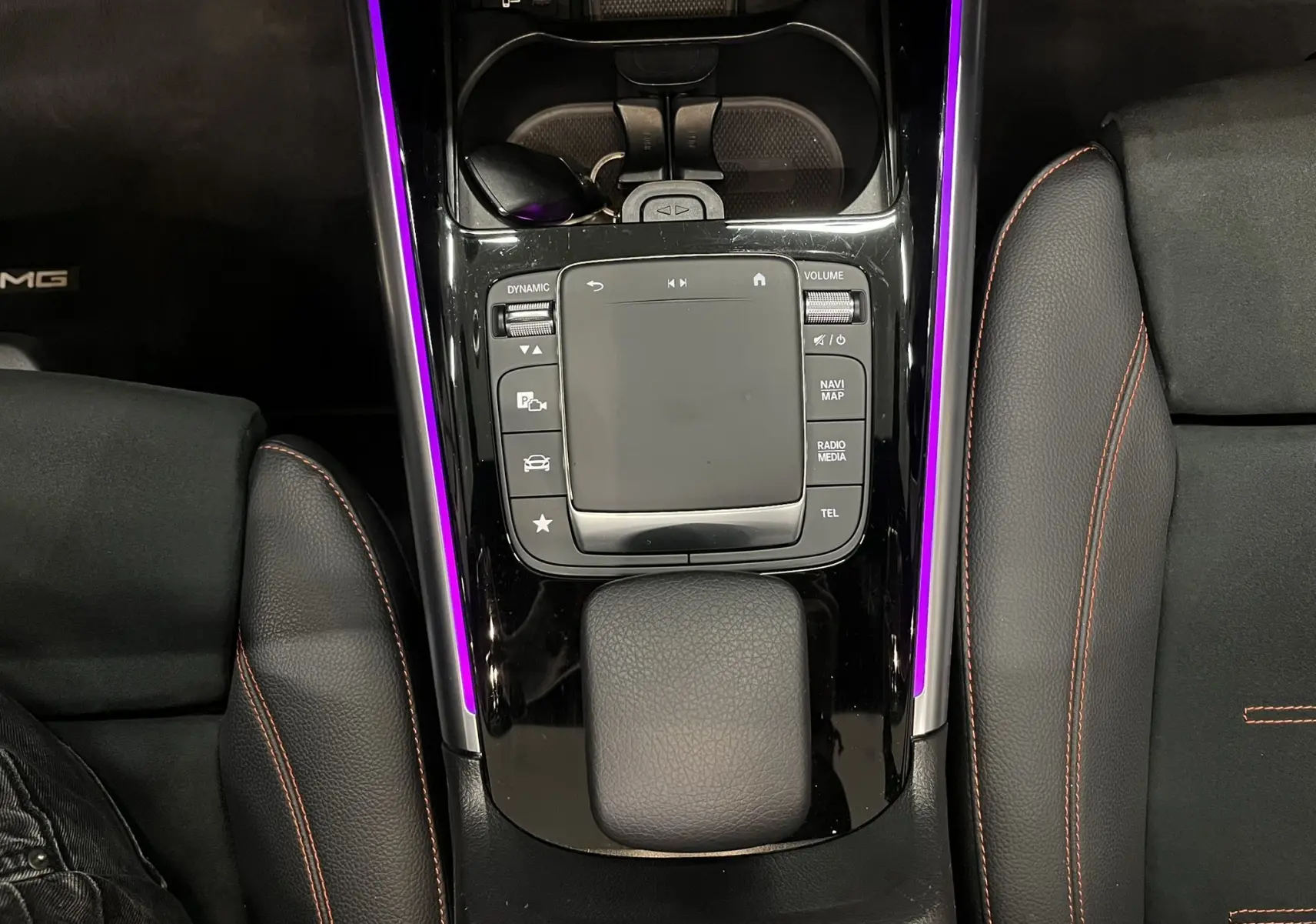Vue plongeante sur la console centrale noire du Mercedes GLA 250E AMG Line avec éclairage d'ambiance violet et surpiqûres rouges.