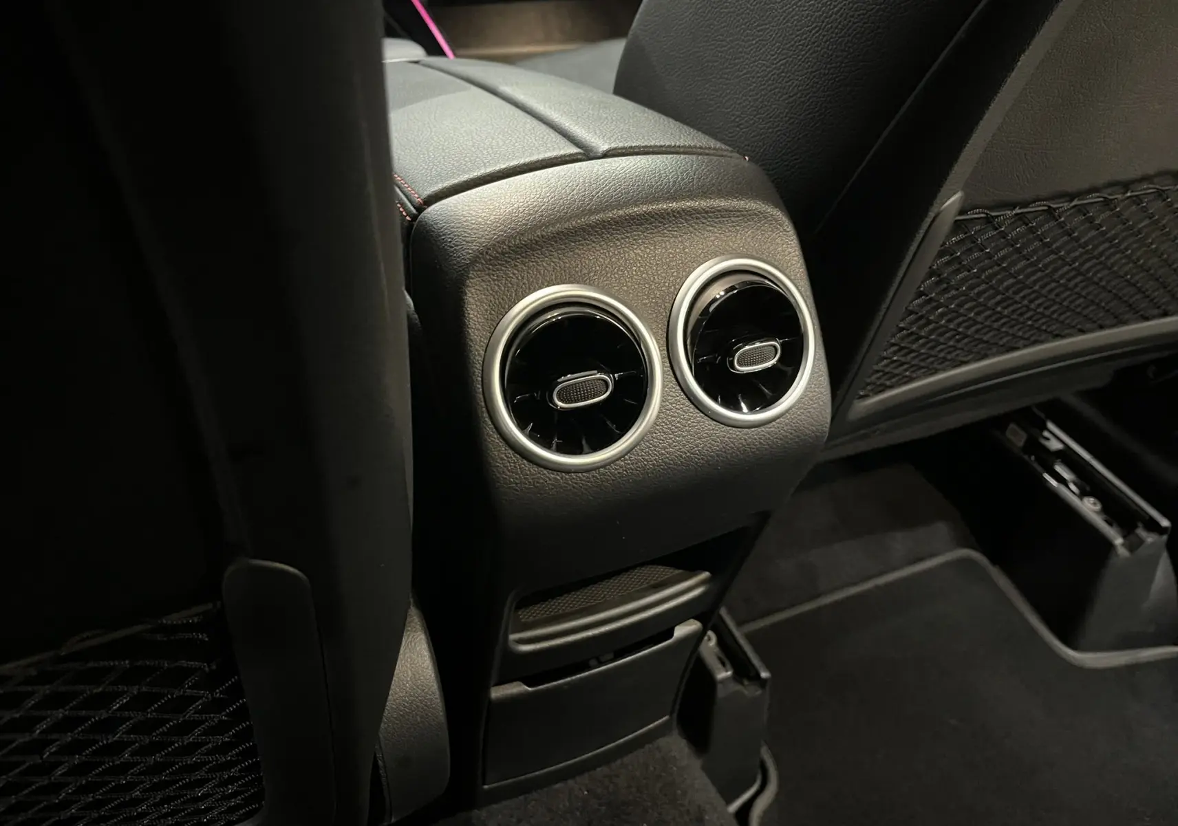 Vue rapprochée des aérateurs arrière et console centrale noire avec surpiqûres rouges dans l'habitacle du Mercedes GLA 250E AMG Line.