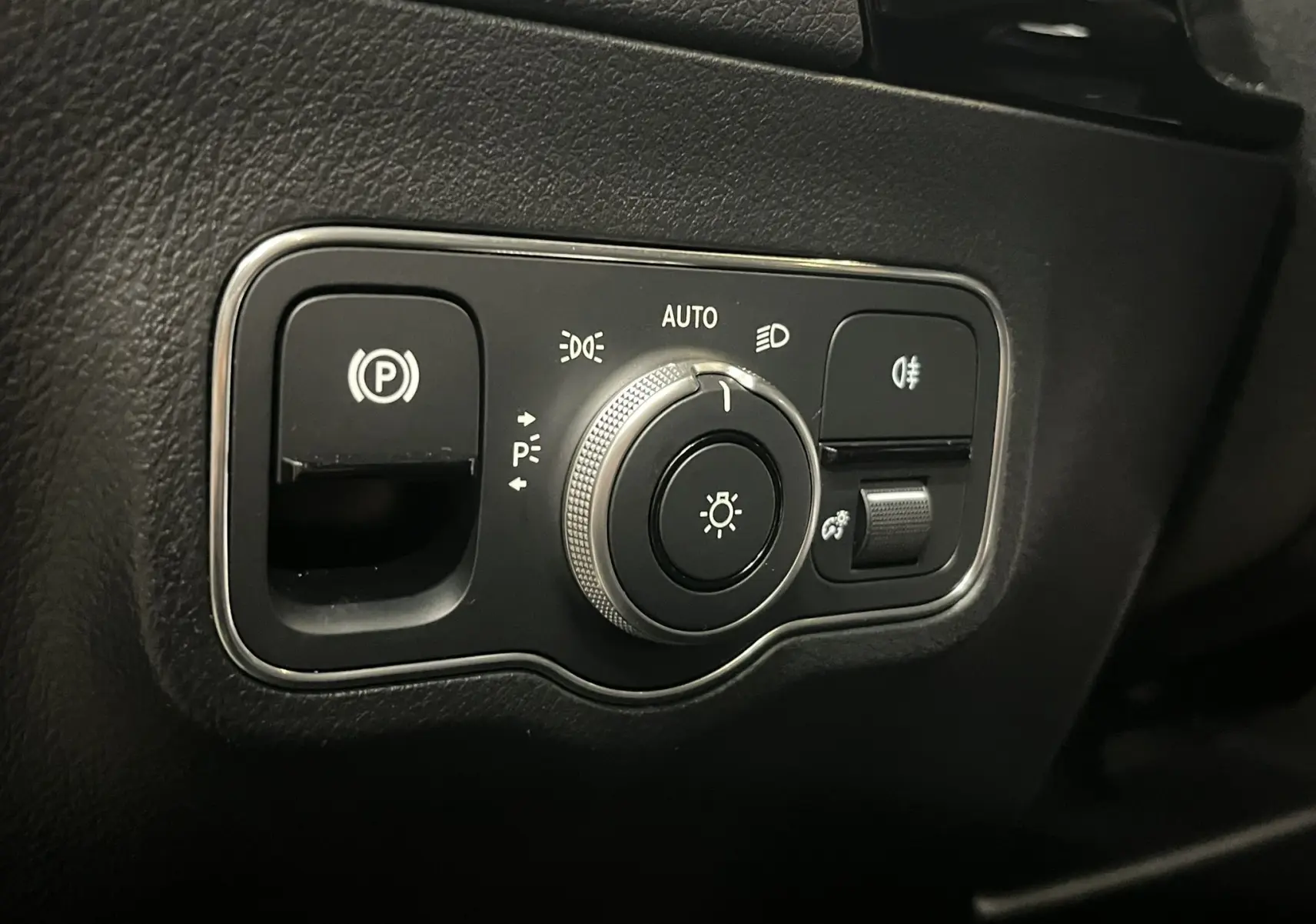 Gros plan sur la commande d’éclairage et frein de stationnement dans l’habitacle noir du Mercedes GLA 250E AMG Line 2023.