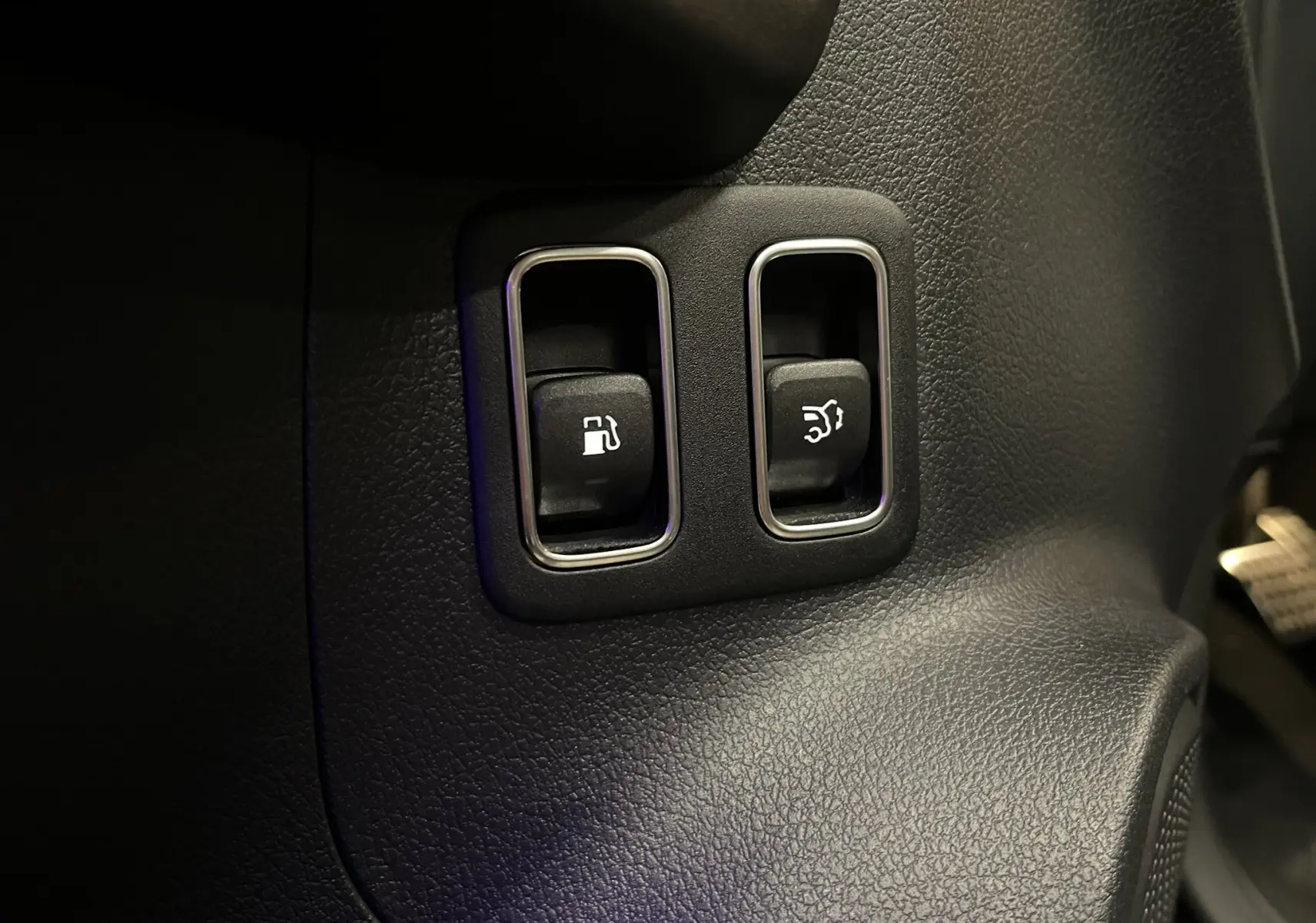 Gros plan sur les boutons d’ouverture de trappe à carburant et de coffre dans l’habitacle noir du Mercedes GLA 250E AMG Line 2023.