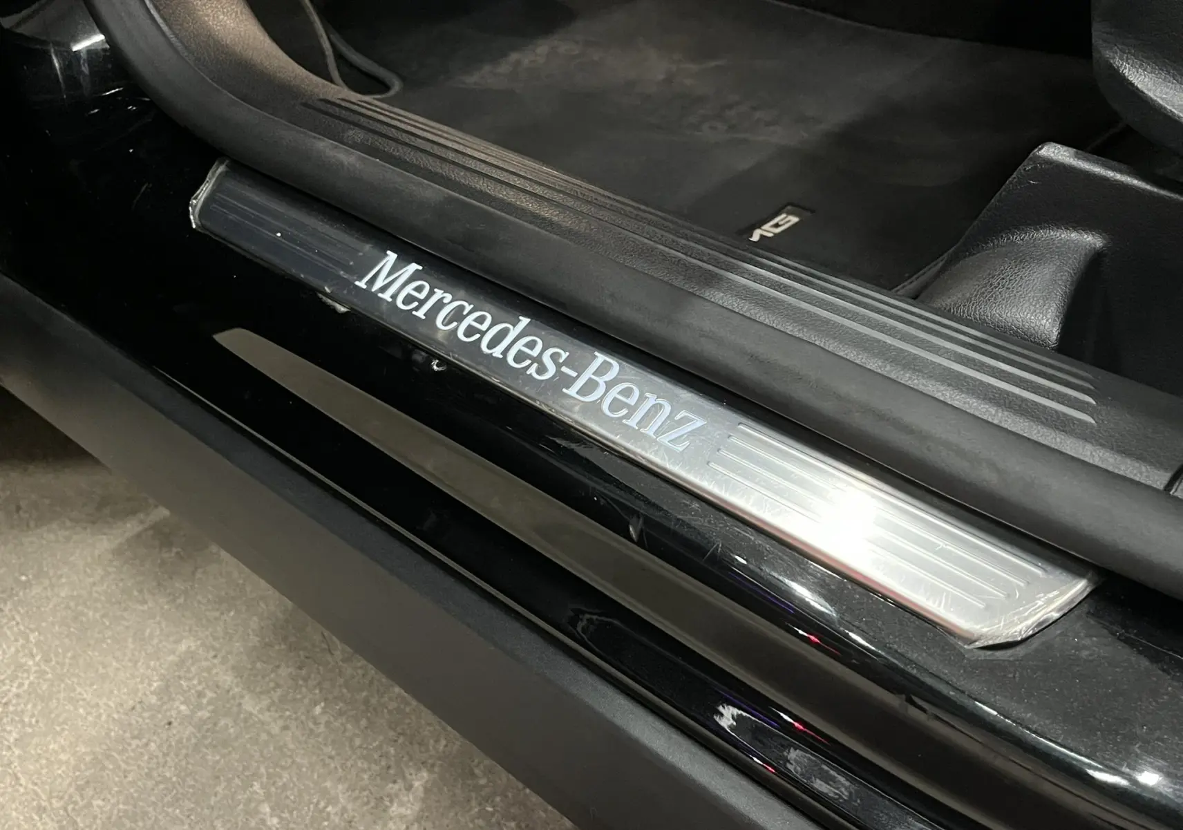 Gros plan sur la baguette de seuil de porte noire Cosmos avec logo Mercedes-Benz éclairé, intérieur noir visible.