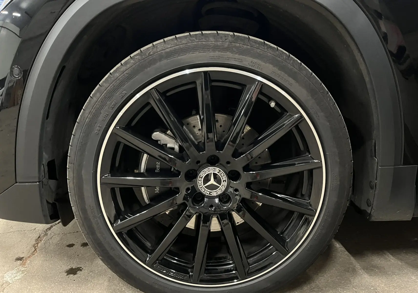 Gros plan sur la roue avant gauche noire avec jante AMG brillante et logo Mercedes au centre.