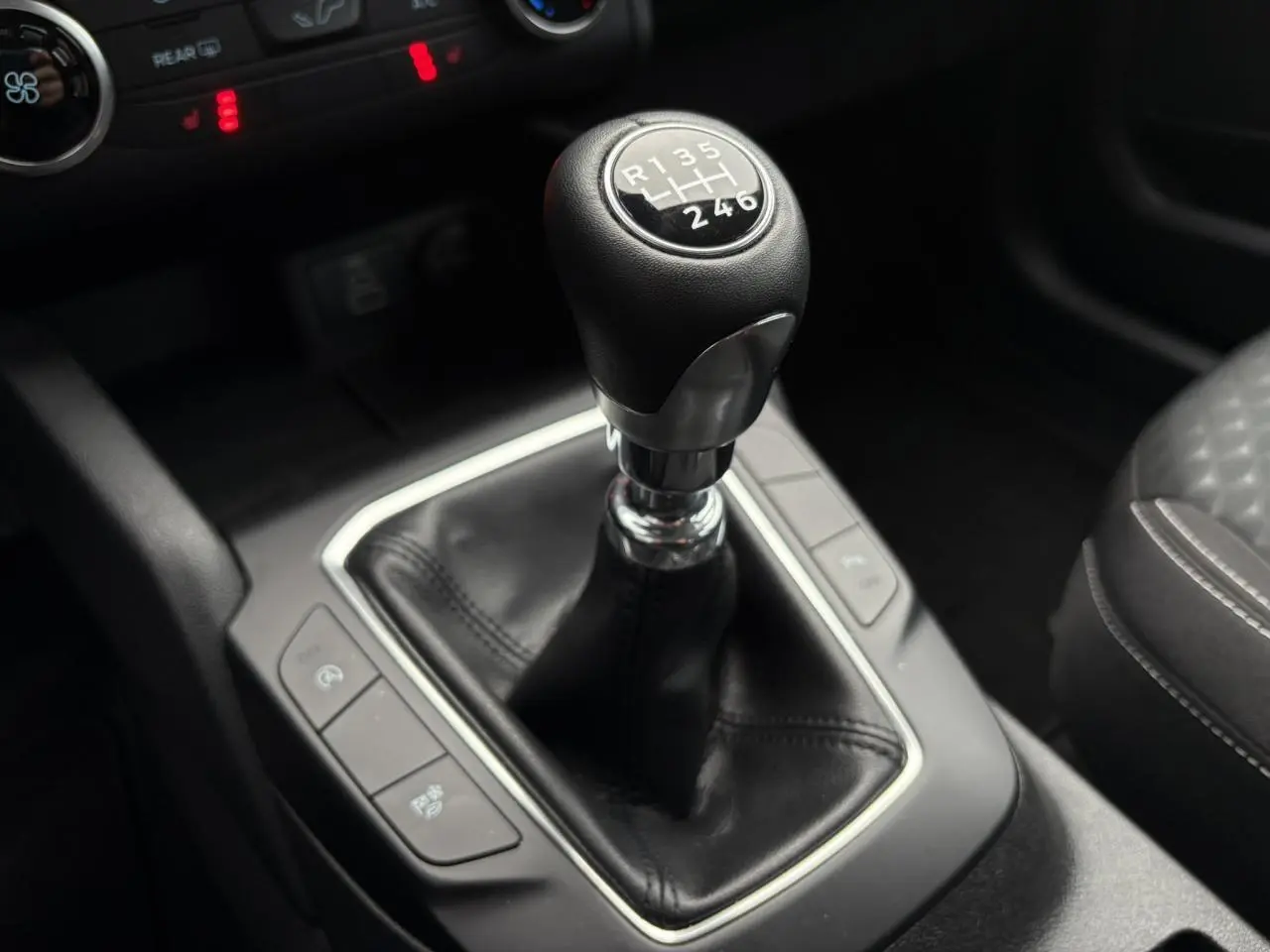 Gros plan sur le levier de vitesses manuel en cuir noir du Ford Kuga 1.5 Ecoboost 2024, intérieur sombre.