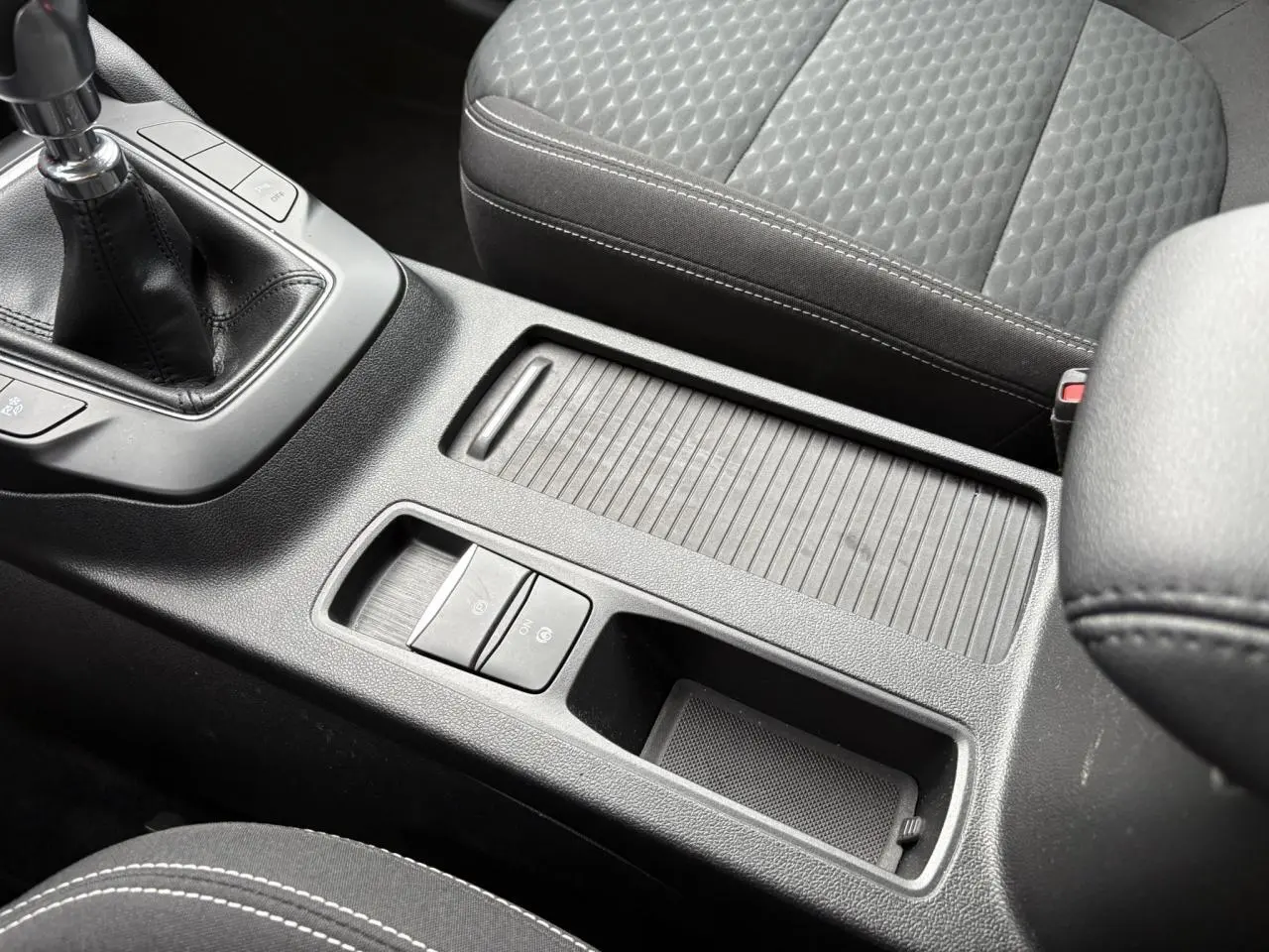 Gros plan sur la console centrale noire du Ford Kuga 2024 avec boîte manuelle et siège avant tissu gris.