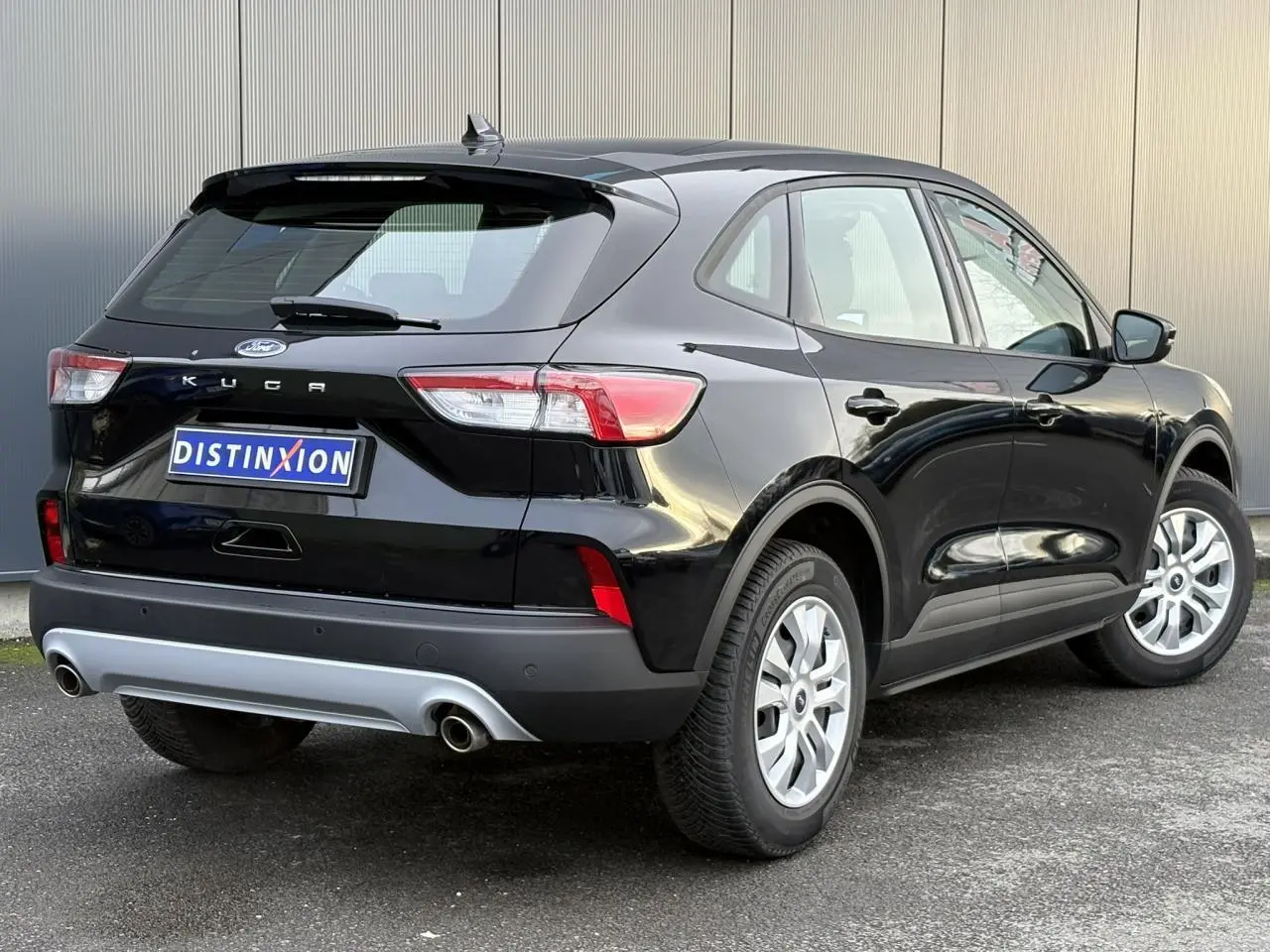Vue 3/4 arrière droite d’un Ford Kuga noir Obsidien 2024 avec double sortie d’échappement et jantes argentées.
