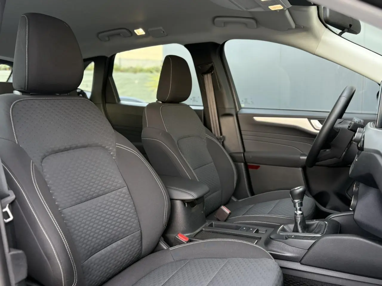 Vue intérieure montrant les sièges avant noirs et la boîte manuelle du Ford Kuga 1.5 Ecoboost 2024 côté conducteur.