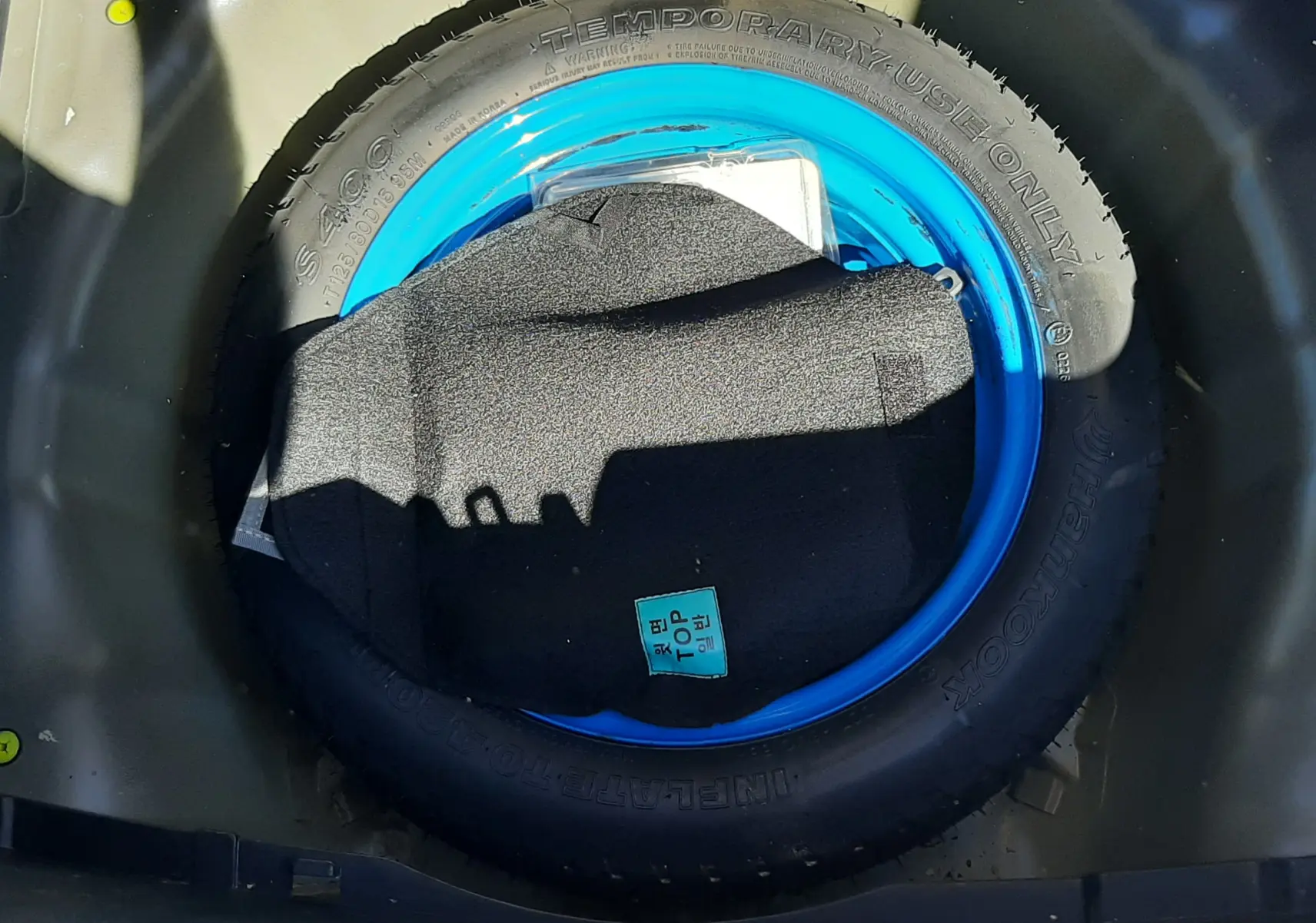 Gros plan sur la roue de secours bleue dans le coffre d'une KIA Rio grise 2016, version essence 1.2 85CH ACTIVE.