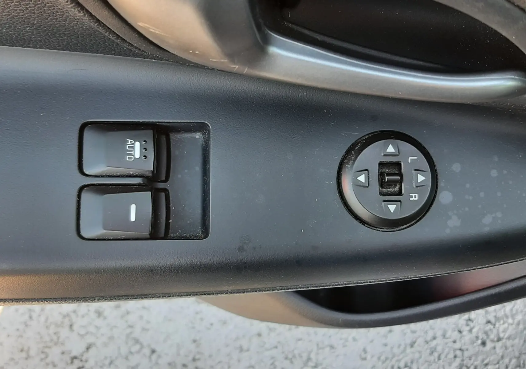 Gros plan sur les commandes de lève-vitres et réglage des rétroviseurs côté conducteur d'une Kia Rio grise 2016.