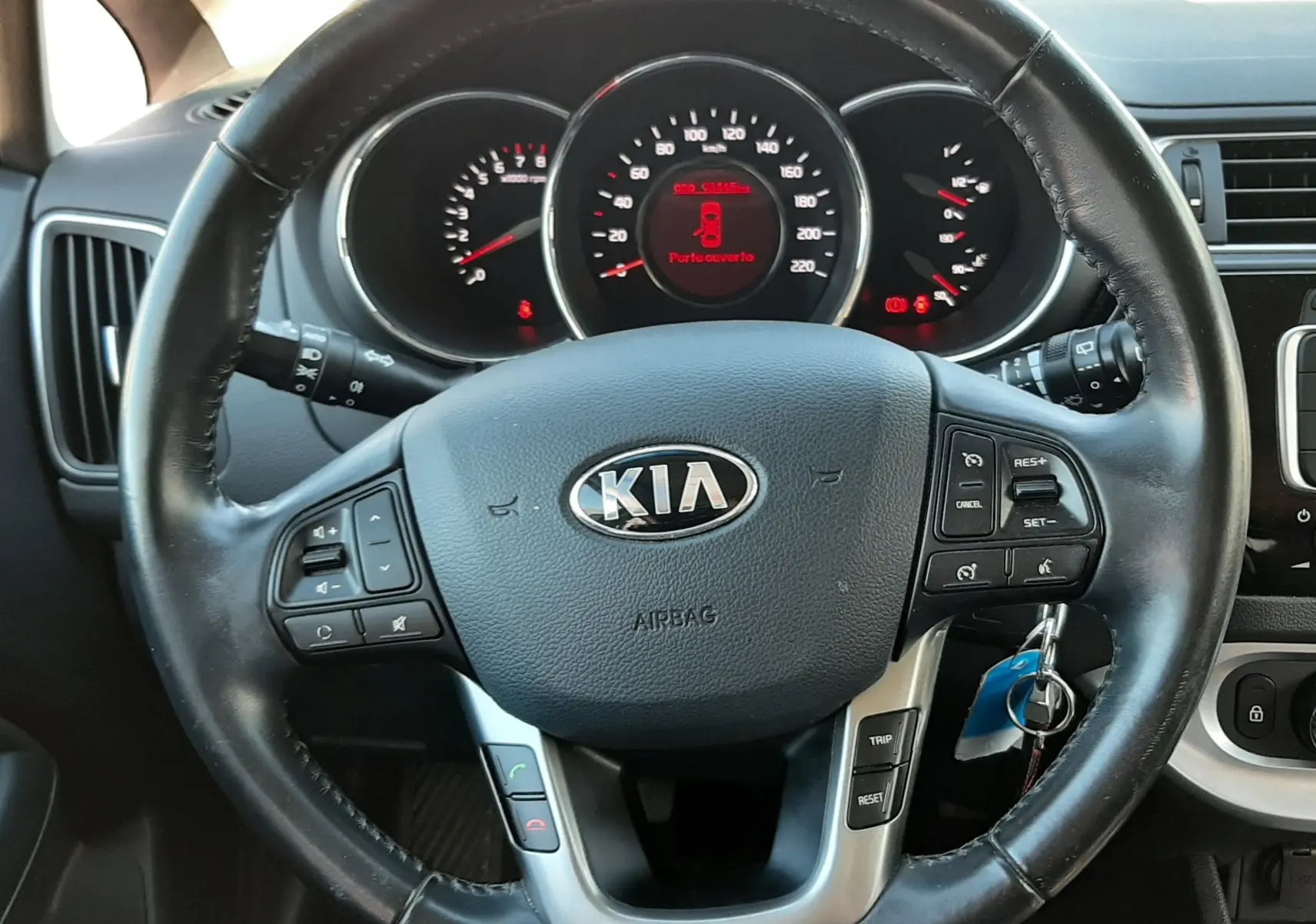 Vue rapprochée du volant noir de la KIA Rio 2016 avec tableau de bord et affichage digital rouge au centre.