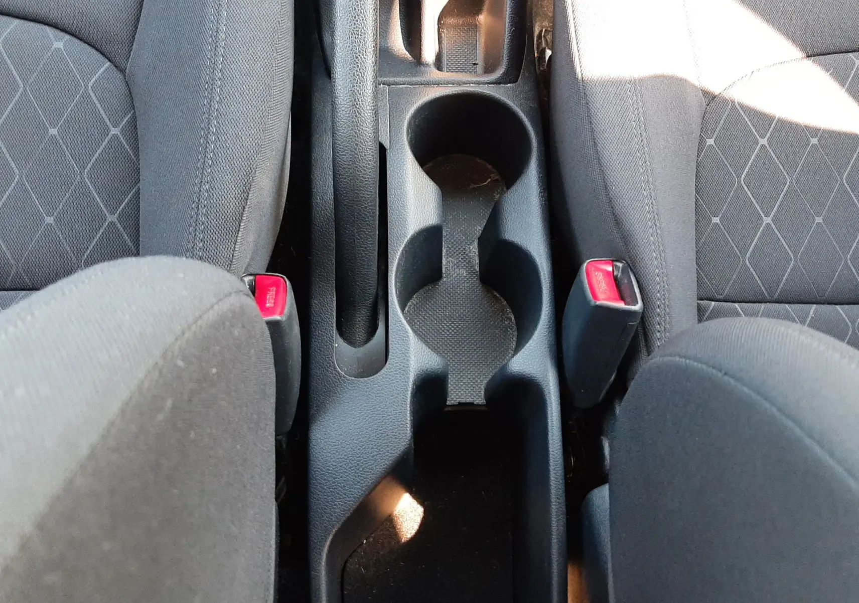 Vue plongeante sur la console centrale noire entre les sièges tissu gris d'une KIA Rio 1.2 85CH ACTIVE 5 portes de 2016.
