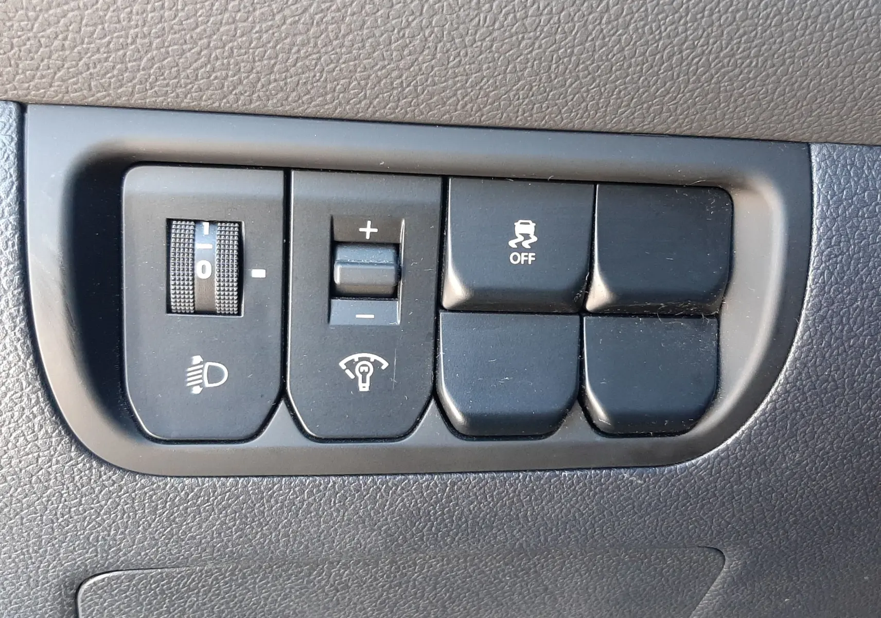 Gros plan sur les commandes de réglage des phares et du tableau de bord d'une KIA Rio grise, version 2016.