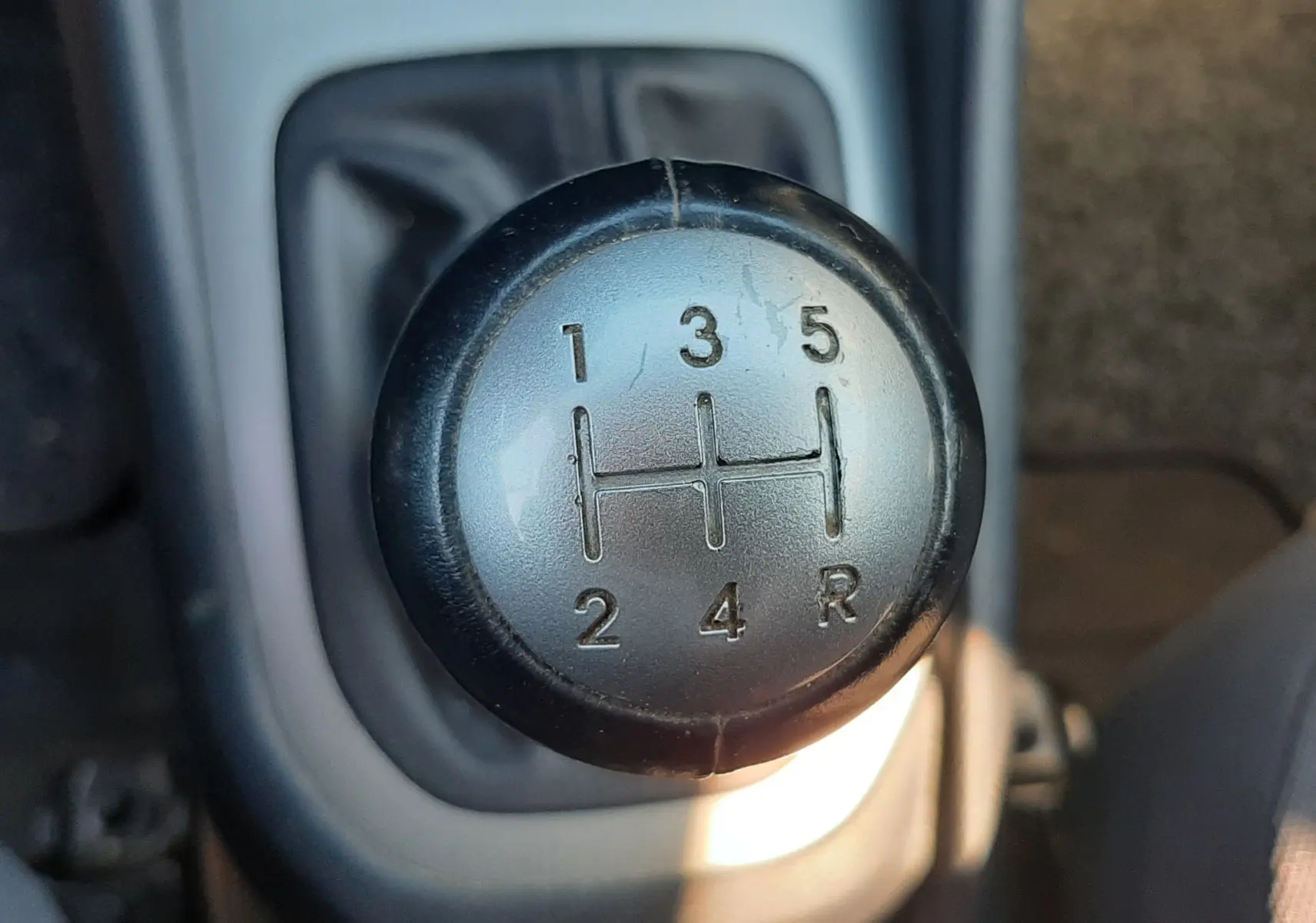 Gros plan sur le pommeau de la boîte manuelle 5 vitesses d'une KIA RIO grise, version 2016, intérieur tissu gris.