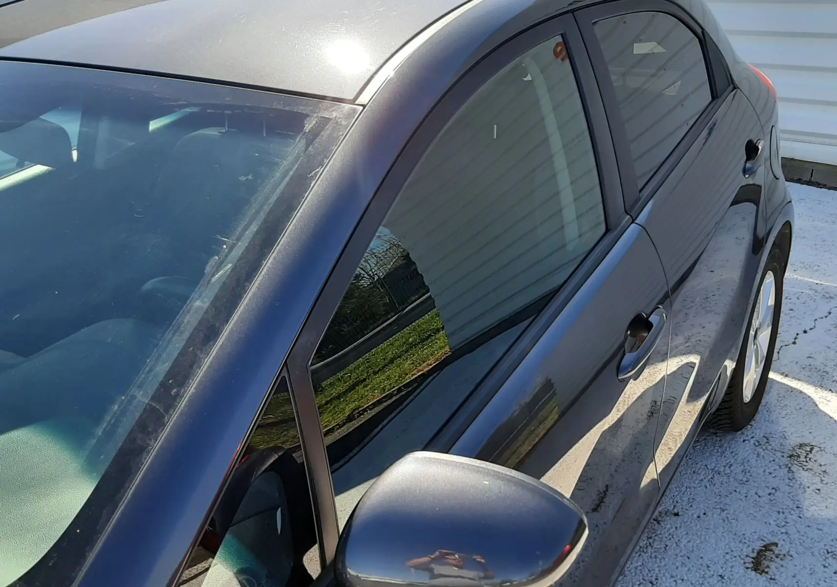 Vue 3/4 avant droit d'une KIA Rio grise 5 portes de 2016 avec rétroviseur électrique et vitres teintées.