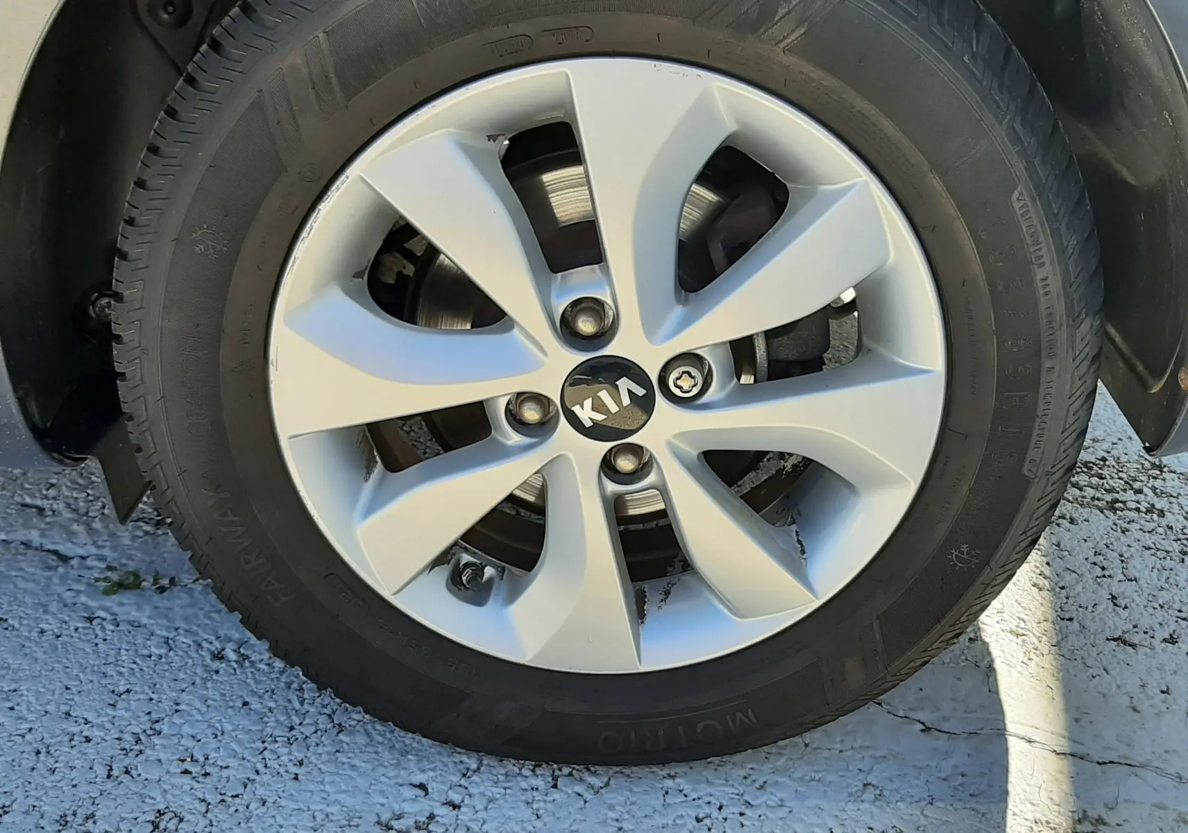 Gros plan sur la roue avant gauche d'une Kia Rio grise de 2016 avec jante alliage et logo central visible.