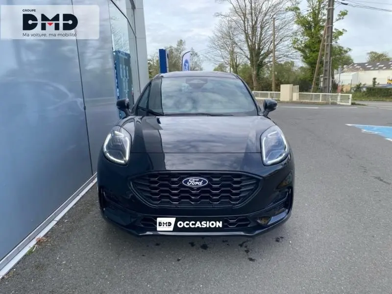 Vue avant d'une Ford Puma noir agate métallisée avec calandre noire et phares LED allumés, stationnée devant un mur gris.